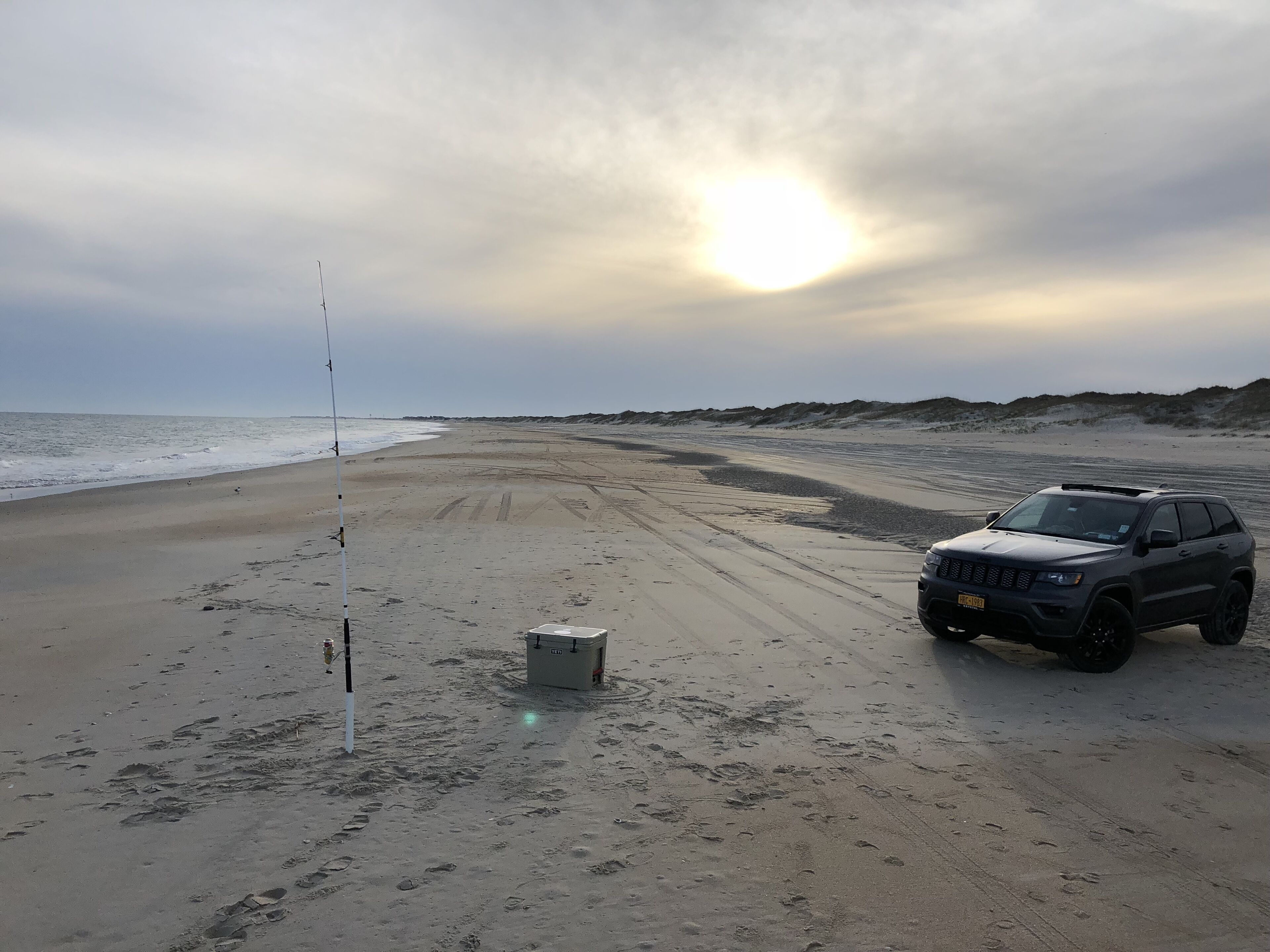 A beach with a fishing rod and a vehicle parked on the sand.