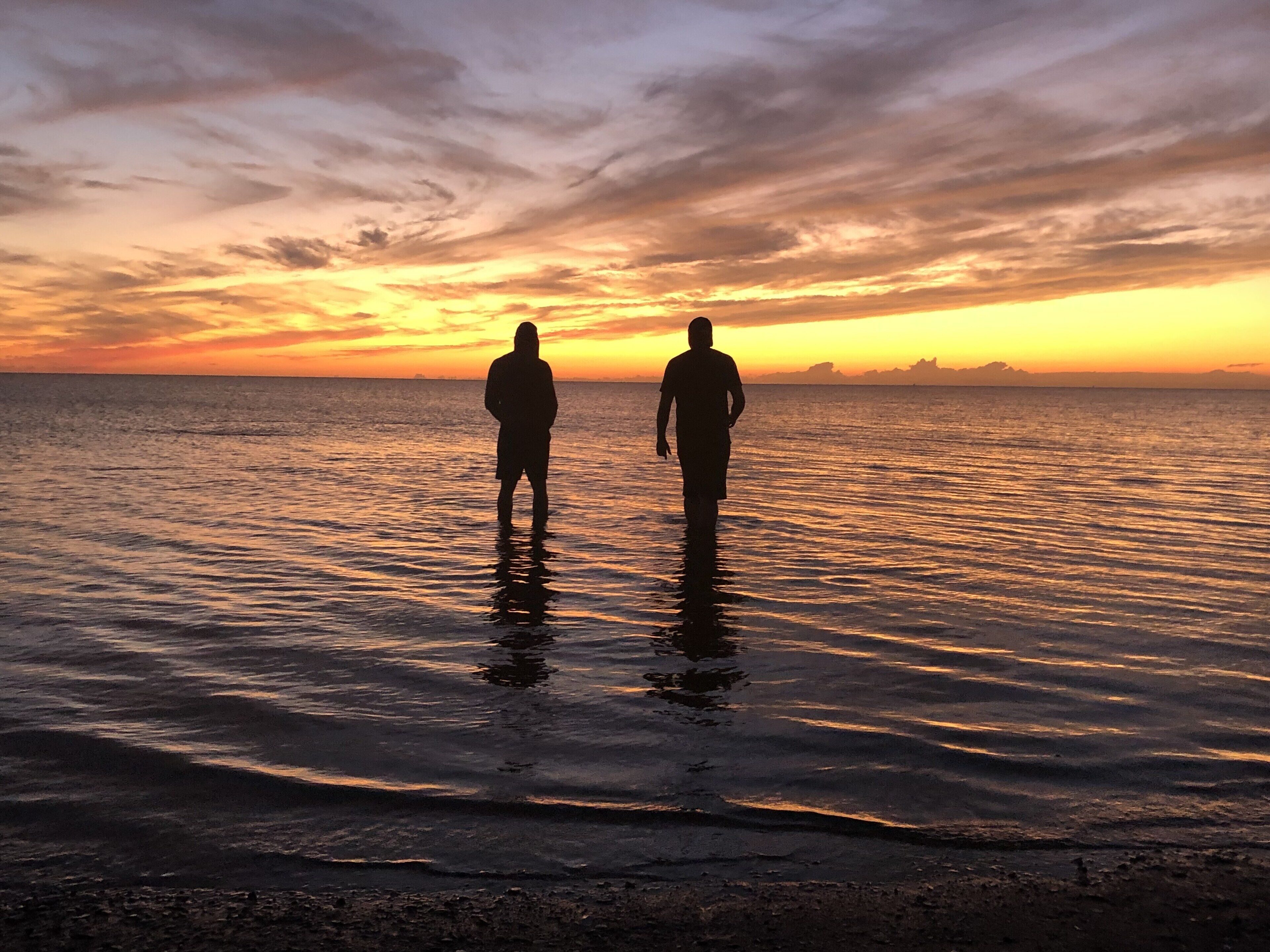 Two people standing in shallow water at sunset.