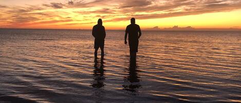 Two people standing in shallow water at sunset.