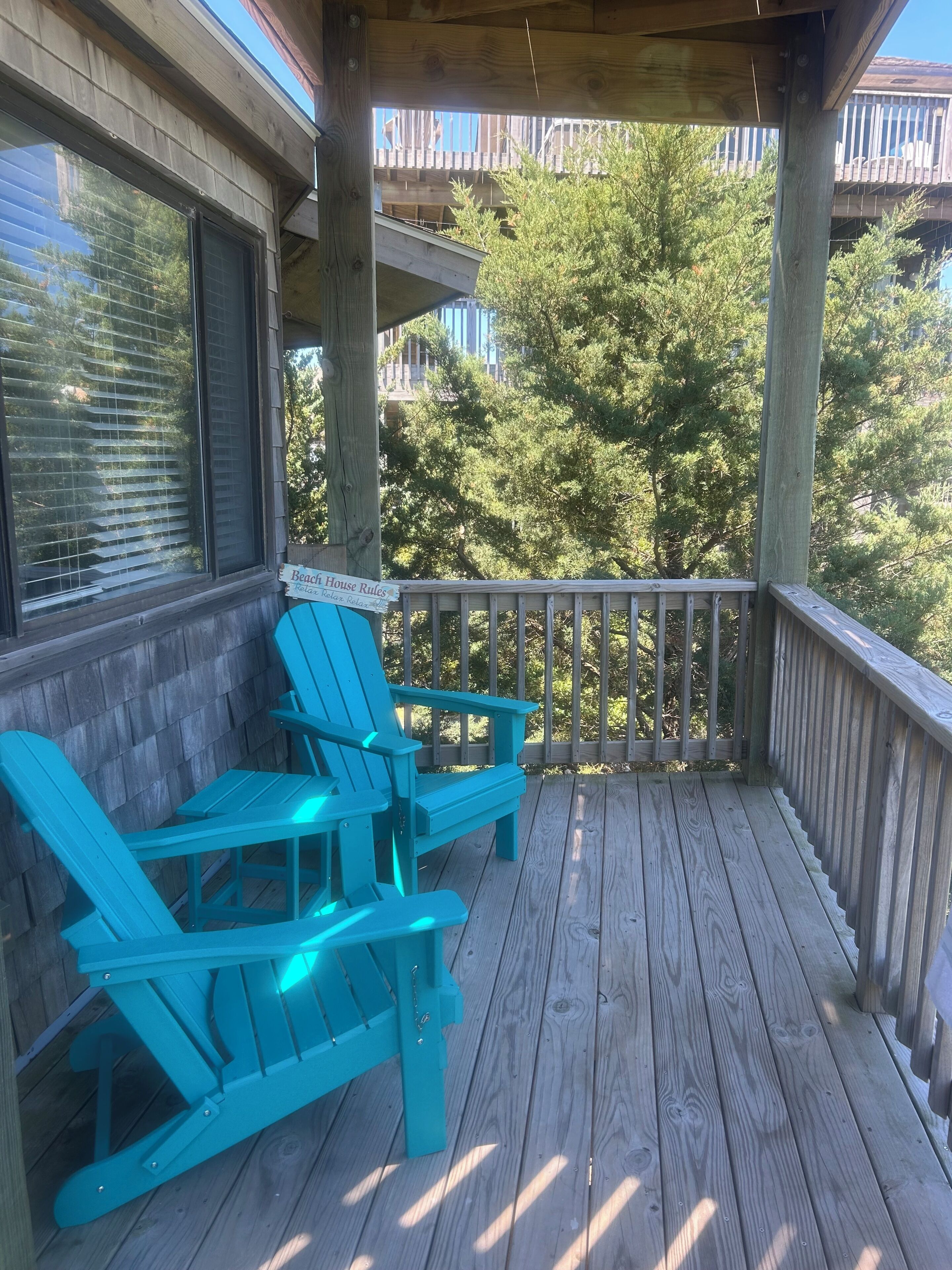 A wooden deck with two turquoise Adirondack chairs and a wooden railing.