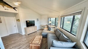 Amplia sala de estar con un gran ventanal, televisor, mesa de centro de madera y sofá.