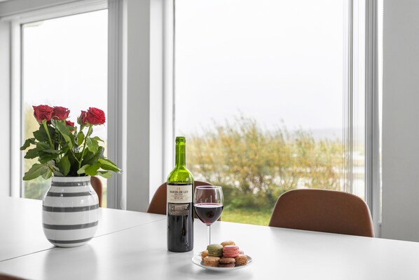 A table with a wine bottle, a glass of wine, a vase with flowers, and macarons. - Luxury Villa with river view In South Iceland - The Golden Circle (Laugarás)