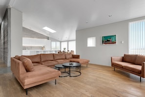 Un amplio espacio de sala con un sofá modular, una mesa de centro redonda y una cocina al fondo.