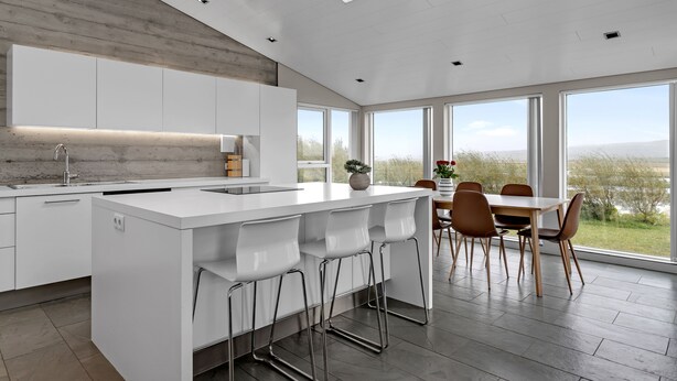 Een moderne keuken met een centraal eiland, een eethoek met tafel en stoelen, en grote ramen met uitzicht op de omgeving.