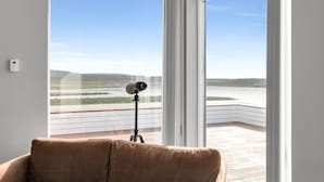 Een kamer met een groot raam met uitzicht op een wateroppervlak en een verafgelegen landschap.