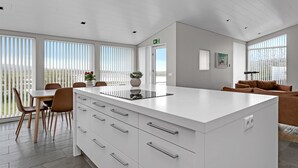 Een moderne keuken met een groot schiereiland, witte kasten en een eethoek met stoelen en een tafel.