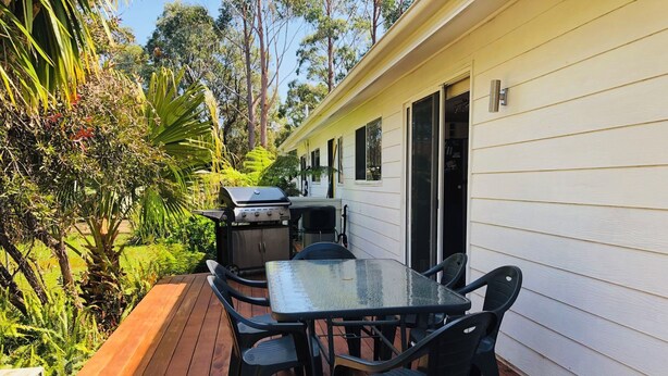 A patio with a table and chairs, a grill, and a wooden deck.