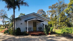 A small, single-story house with a porch, surrounded by greenery and trees.