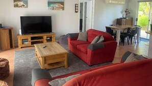 A living room with a red sofa, a television on a wooden stand, and a dining area with a table and chairs.