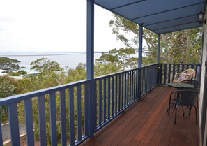 Una terraza de madera con barandilla azul, con vista a un cuerpo de agua y árboles.