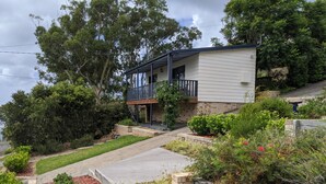 A two-story house with a balcony, surrounded by a landscaped garden and trees.