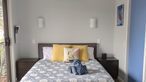 A bedroom with a bed, a bedside table, a nightstand, a wall-mounted air conditioner, and a door.