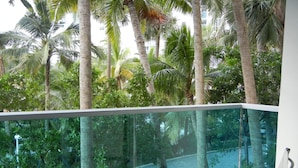 Ein Balkon mit Glasgeländer mit Blick auf einen Strand mit Palmen.
