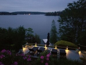 A deck with lounge chairs and tables, overlooking a body of water with distant lights.