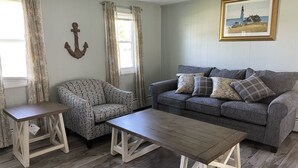 A living room with a grey sofa, patterned armchair, and a wooden coffee table. - Walk to Beach with with central AC! (Narragansett)