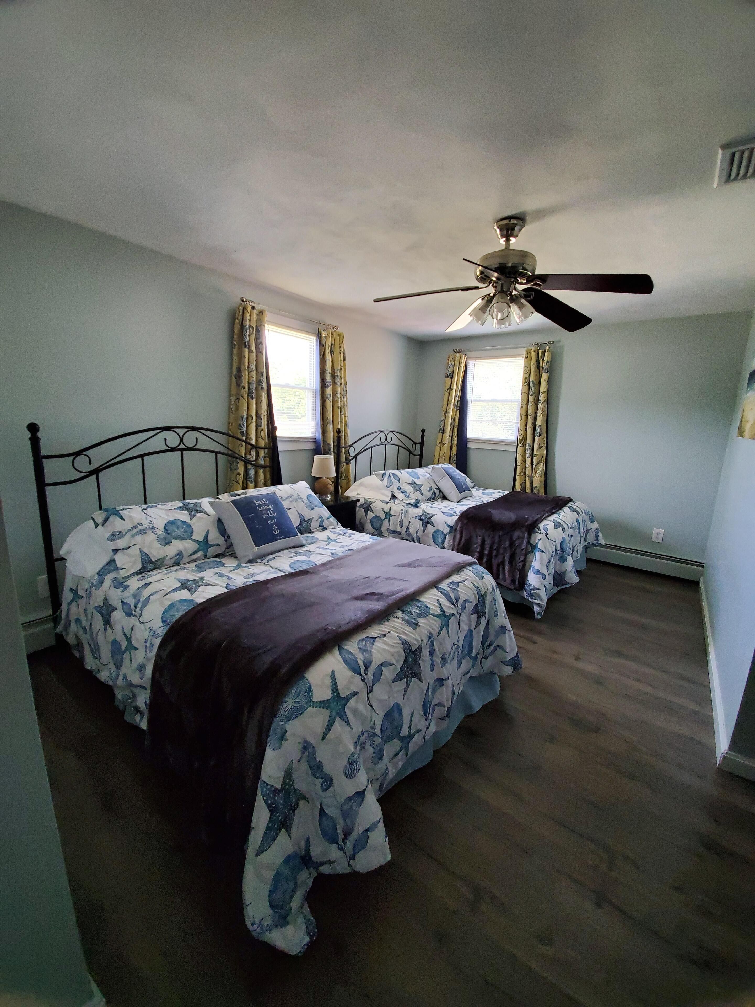 Une chambre avec deux lits, un ventilateur de plafond et des fenêtres avec des rideaux.