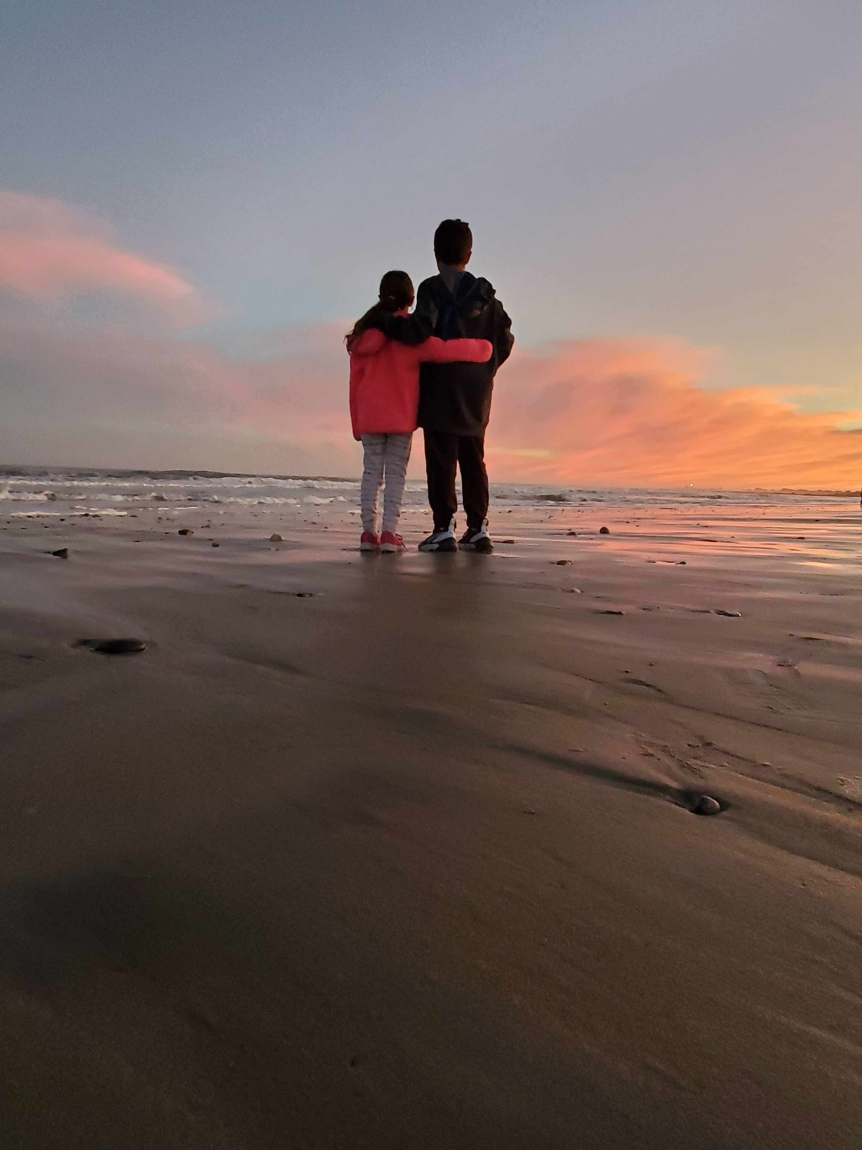 Two people standing on a beach with a sunset in the background.