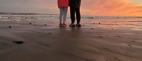 Two people standing on a beach with a sunset in the background.