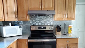 A kitchen with wooden cabinets, a stainless steel oven, a microwave, and a tiled backsplash. - Walk to Beach with with central AC! (Narragansett)