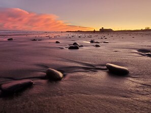 A beach with scattered rocks and a distant structure. - Walk to Beach with with central AC! (Narragansett)