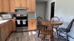 A kitchen with wooden cabinets, a microwave, an oven, and a dining table with four chairs. - Walk to Beach with with central AC! (Narragansett)