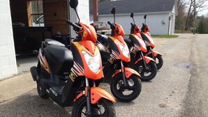Drei Kymco-Roller sind hinter einem Gebäude in einer Reihe abgestellt.