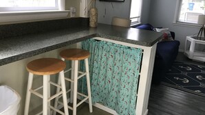 Eine Küche mit einer Granit Arbeitsplatte, zwei hölzernen Barhocker, einer Vase mit Trockenpflanzen und einem gemusterten Vorhang.