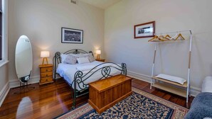 A bedroom with a bed, bedside lamps, a wooden bench, a hanging clothes rack, and a mirror.