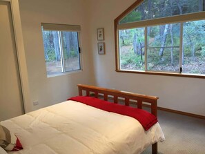 A bedroom with a bed, a window with a view of trees, and a door.
