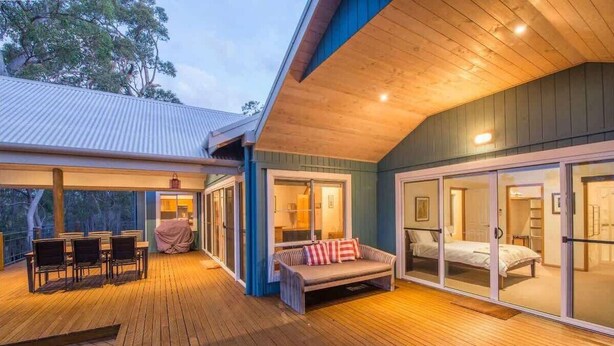 A wooden deck with outdoor seating, a covered area, and a bedroom with sliding glass doors. - Burwood Bush House—Close to Wineries and Beach (Yallingup Siding)