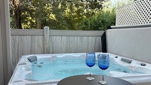 A hot tub with two glasses of blue liquid, surrounded by a wooden deck and a white fence.