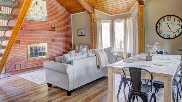 A cozy living room with a fireplace, a dining area with a wooden table and chairs, and a large wall clock.