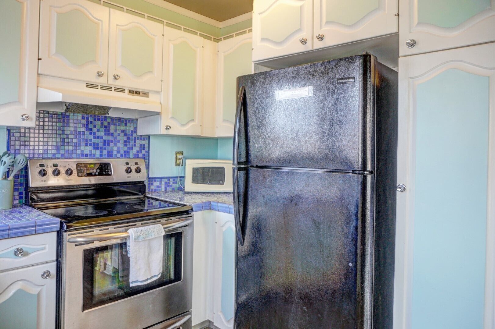 A kitchen with white cabinets, a black refrigerator, a stove, and a microwave.