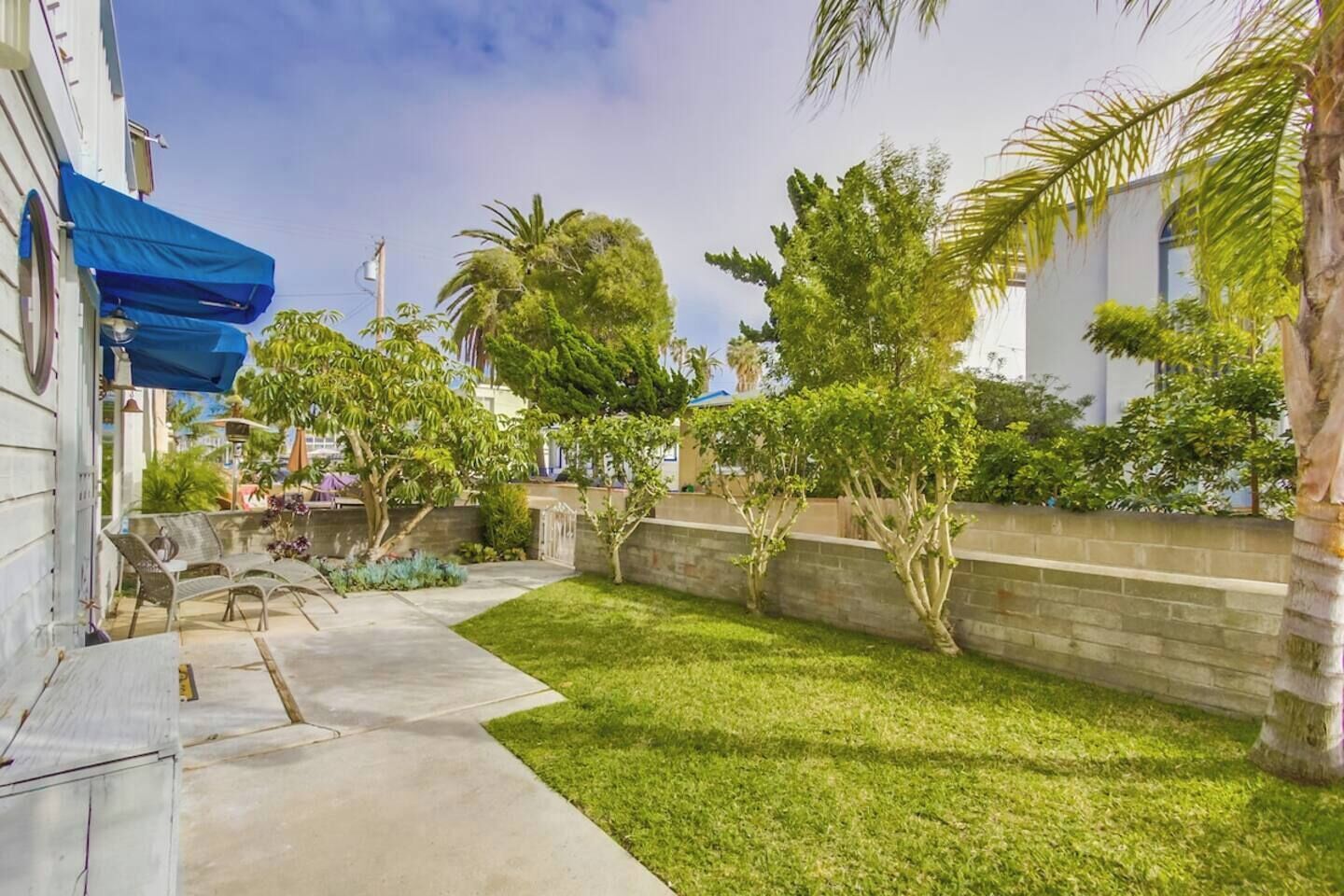 Un espace extérieur aménagé avec soin, comprenant une terrasse, un sol en béton, une pelouse et une variété d’arbres et d’arbustes.