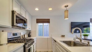 A modern kitchen with stainless steel appliances, a window with blinds, and a flat-screen TV mounted above the sink. - MB Bungalow steps to the bay for pets with bikes (San Diego)