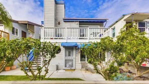 A two-story residential building with a balcony, a garage door, and a small front yard with potted plants. - MB Bungalow steps to the bay for pets with bikes (San Diego)