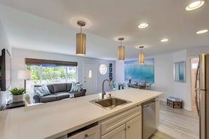 A modern kitchen with a central island, pendant lights, and a dining area with a view of the outdoors.