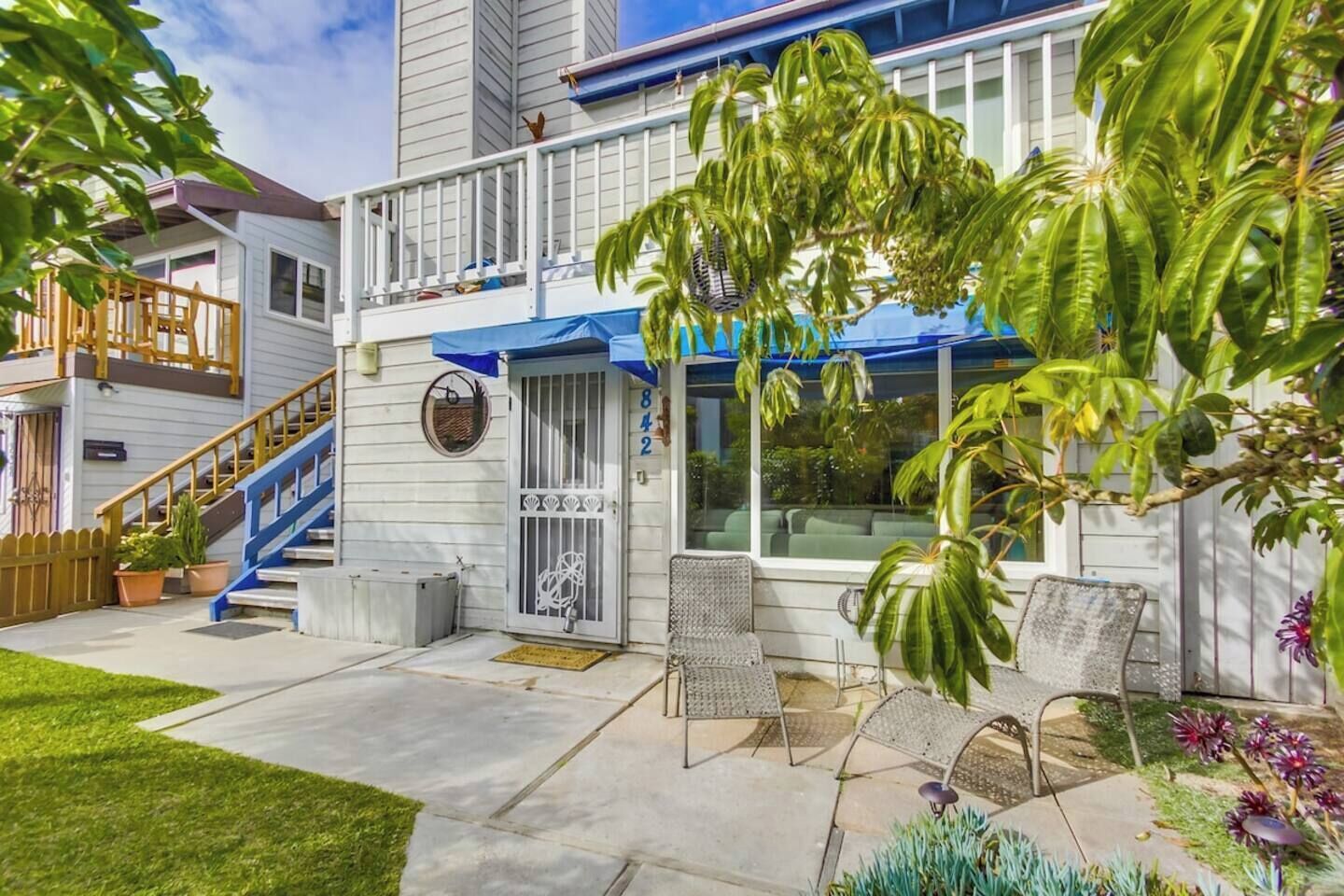 A two-story house with a blue staircase, a covered porch, and a small garden with potted plants and a bird feeder.