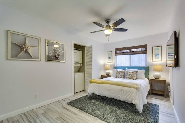A bedroom with a bed, a ceiling fan, a window with blinds, and a door leading to a laundry area.