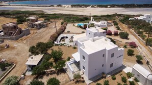 Zona residencial costera con edificios blancos modernos, una playa arenosa y un cielo azul despejado.