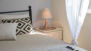 Una cama bien hecha con ropa de cama estampada, una lámpara de noche y una ventana con cortinas de gasa.