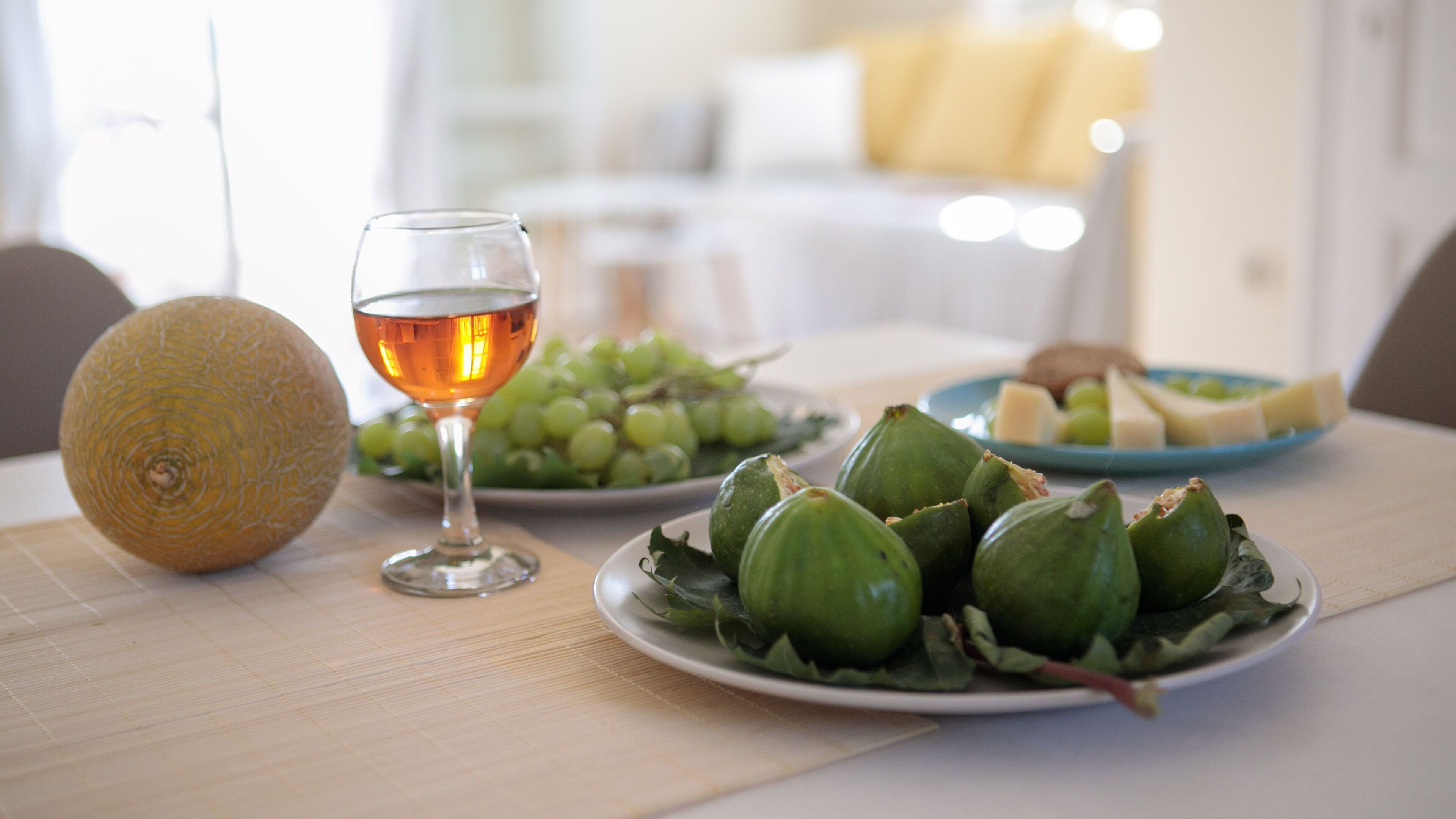 A table with a glass of wine, a plate of green grapes, a plate of cheese, and a melon.