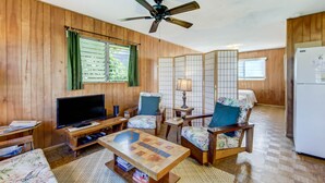 Una habitación con paneles de madera, televisión, una mesa de centro, dos sillas, una lámpara y un refrigerador.