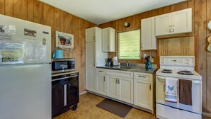 Una cocina compacta con paredes de madera, armarios blancos, una estufa y un refrigerador.