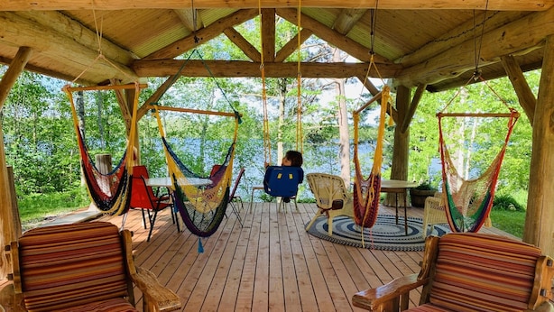 Eine Holzterrasse mit Hängematten und gestreiften Stühlen, mit Blick auf eine natürliche Landschaft.