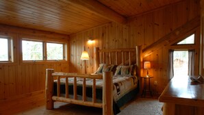 Ein Zimmer in einer Holzhütte mit einem Bett, einem Schreibtisch und einem Fenster mit Vorhängen.