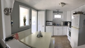A kitchen with white cabinets, a microwave, a refrigerator, and a dining table with a red cushion.