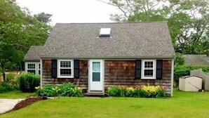 A single-story house with a sloped roof, a front porch, and a small garden area with flowers and shrubs.
