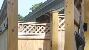 A wooden deck with a lattice top rail, a metal gate, and a hose running along the deck.