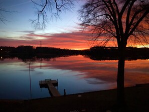A serene sunset over a calm lake with a dock and a tree in the foreground. - Lake House with amazing lake views (Inman)